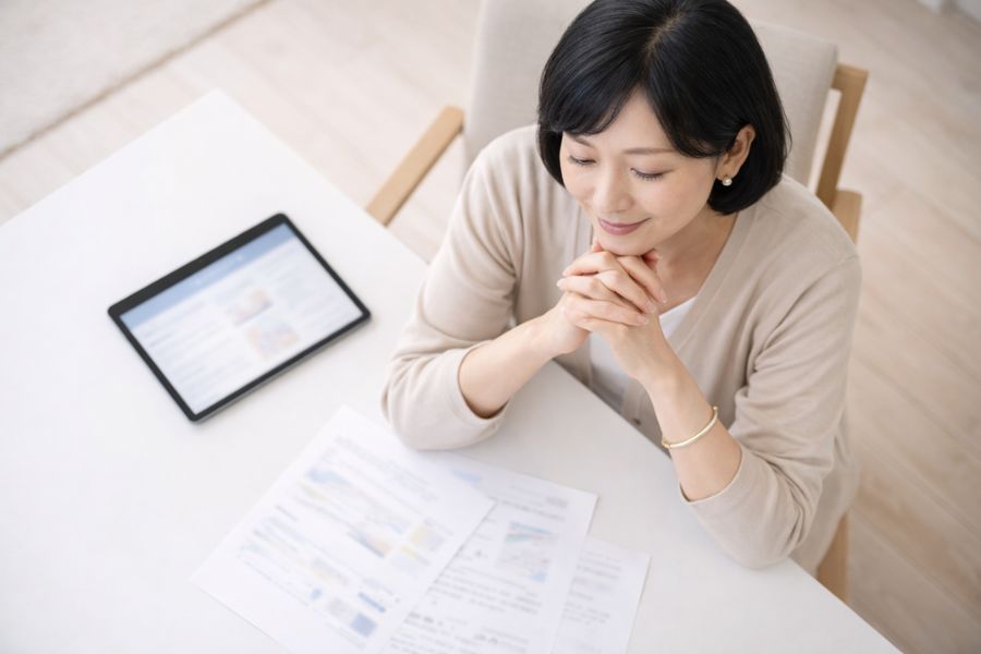 テーブルの上の資料とタブレットを見比べる女性を真上から撮影した様子
