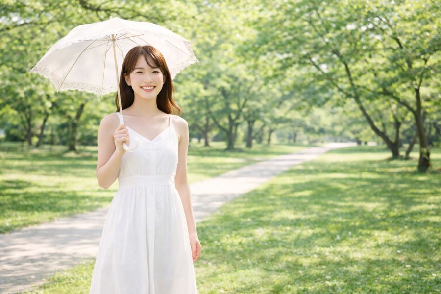 公園の木漏れ日の中で爽やかに立つ20代女性の全身