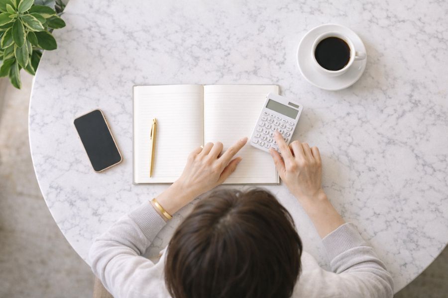 カフェのテーブルでノートと電卓を広げる女性の俯瞰ショット