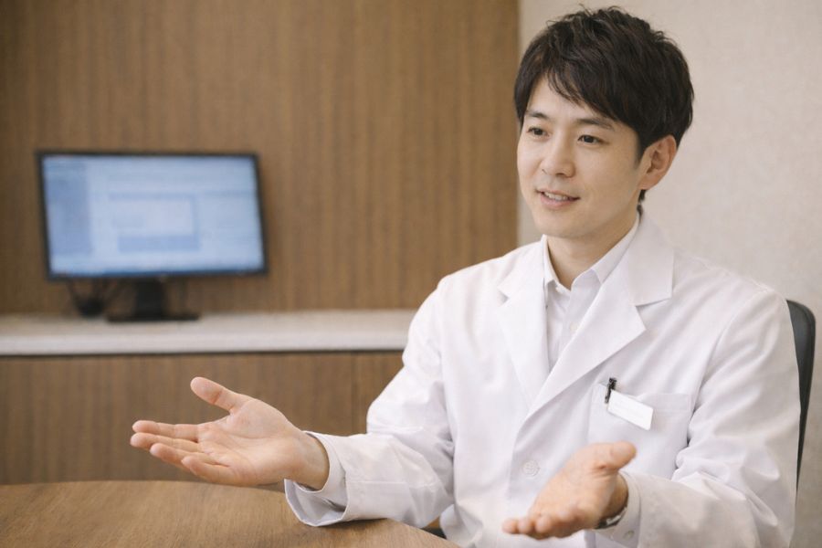 診察室で両手を開いて説明する眼鏡の男性医師