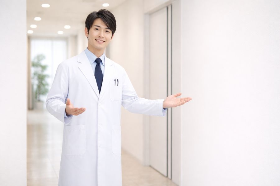 クリニックの廊下で両手を広げて案内する若い男性医師