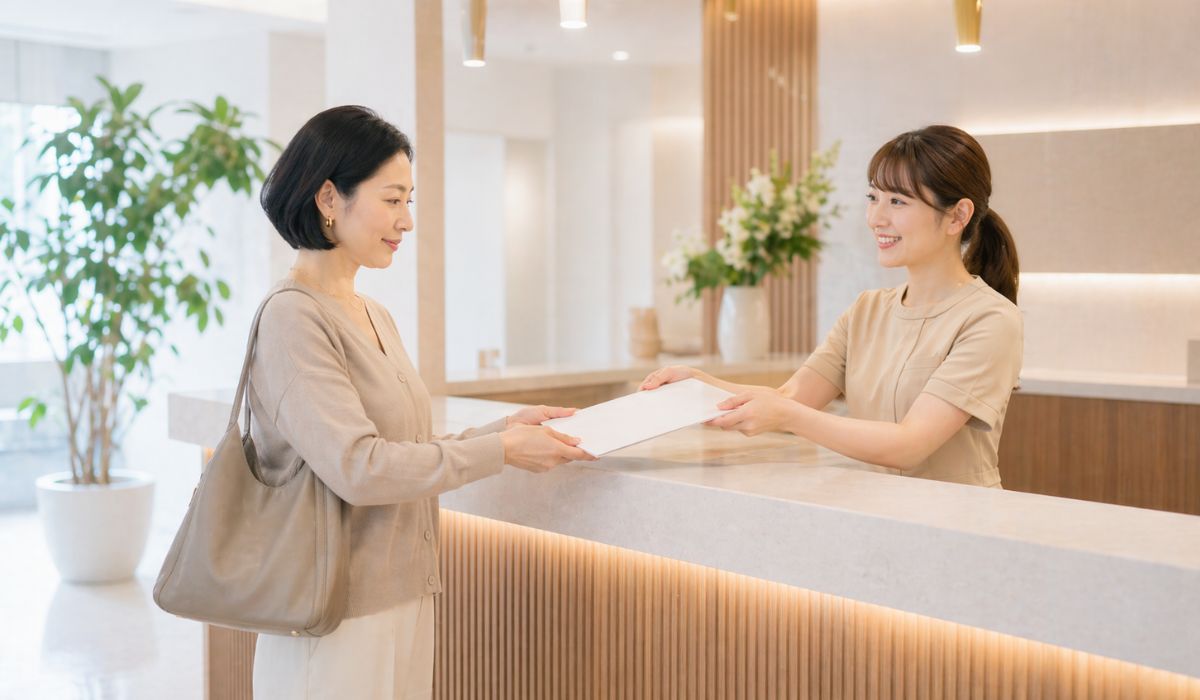 クリニック受付で書類を受け取る女性と渡すスタッフ