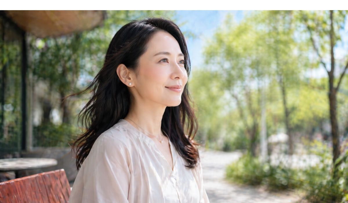 屋外のベンチで遠くを見つめて穏やかに微笑む女性