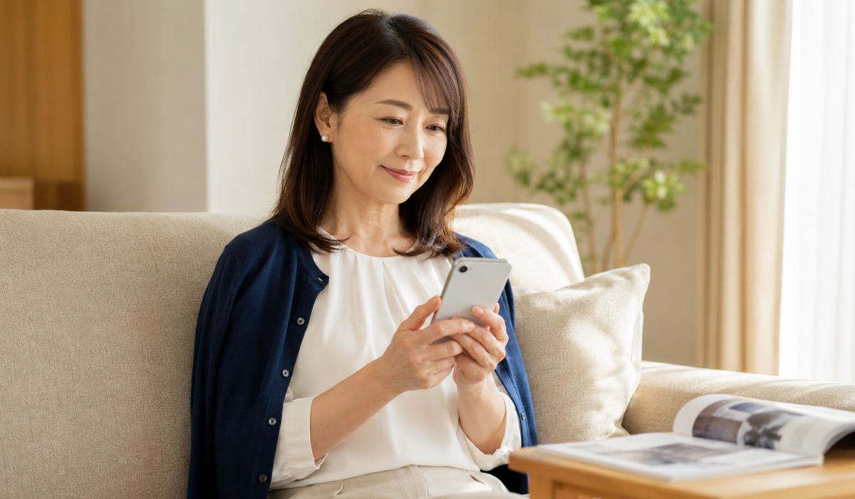 リビングのソファでスマートフォンを見て情報を調べる50代前半の日本人女性
