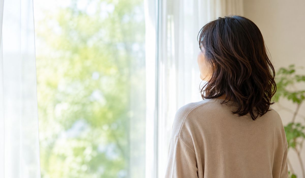 自宅の窓辺で外を眺める女性の後ろ姿