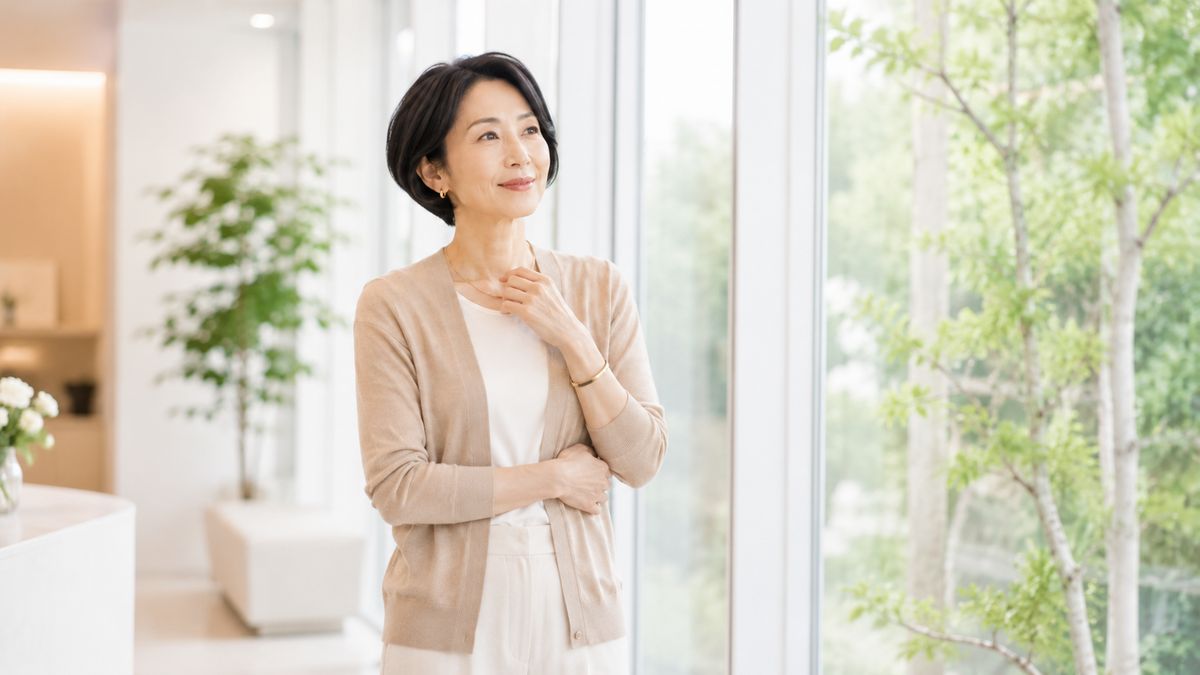 窓辺に立ち前を向いてほほ笑む女性