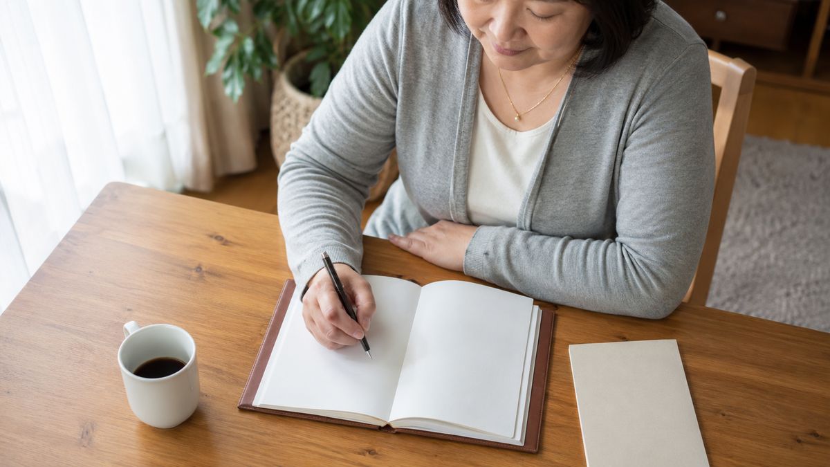 自宅のテーブルで手帳に書き込む女性を上から見た様子