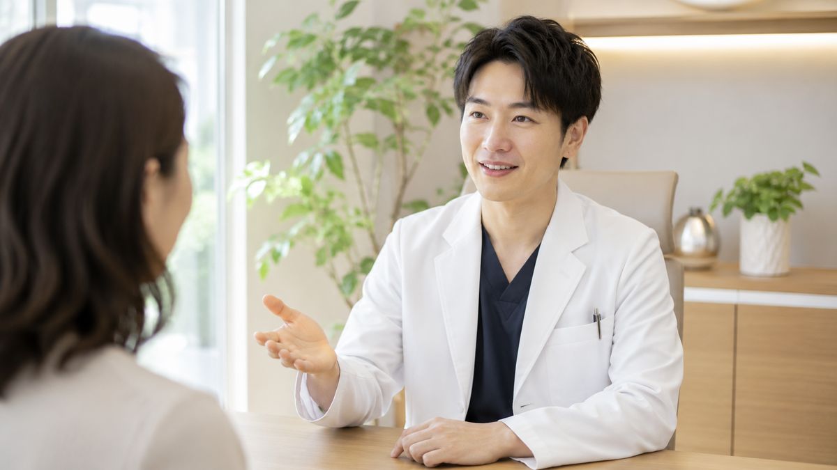 診察室のデスクで手ぶりを交えて話す男性医師