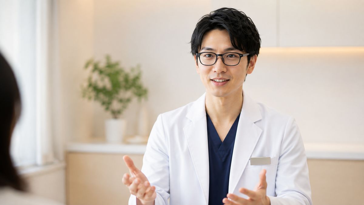 診察室で正面を向いて話す眼鏡の男性医師