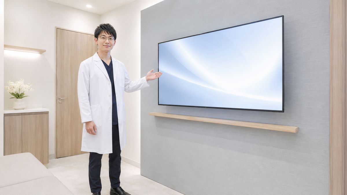 モニターの横に立って話す眼鏡をかけた男性医師