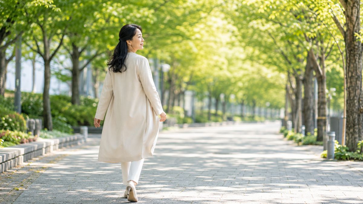 木漏れ日の並木道を歩く女性の後ろ姿