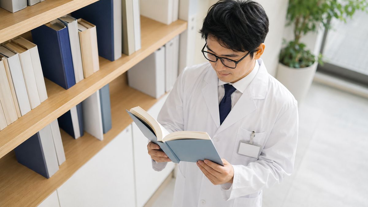 書棚から本を取り出して開く白衣の男性医師