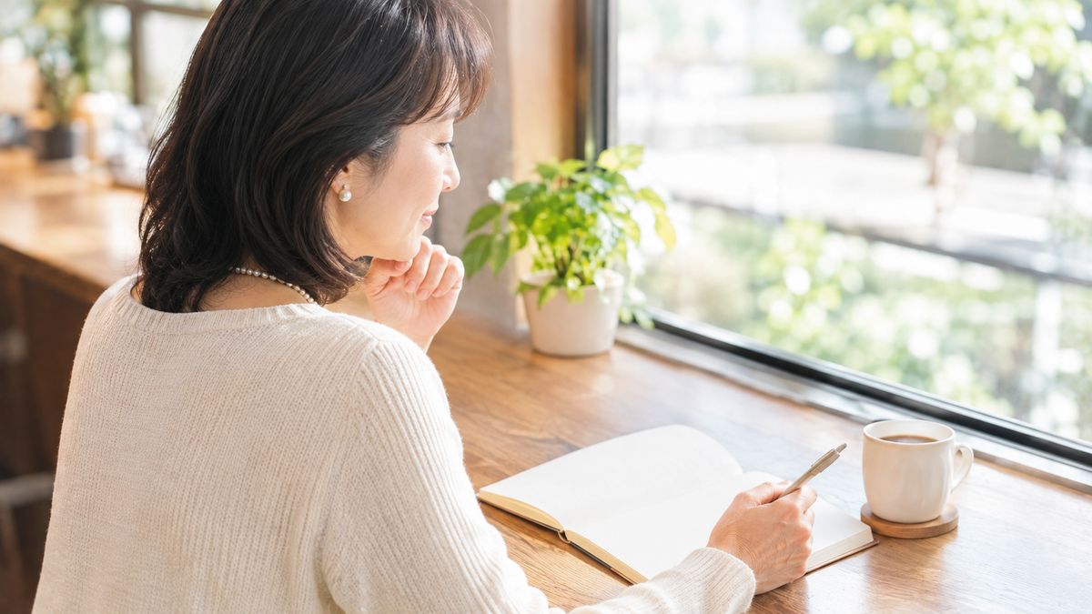 カフェのカウンター席でノートを開いている女性の後ろ姿