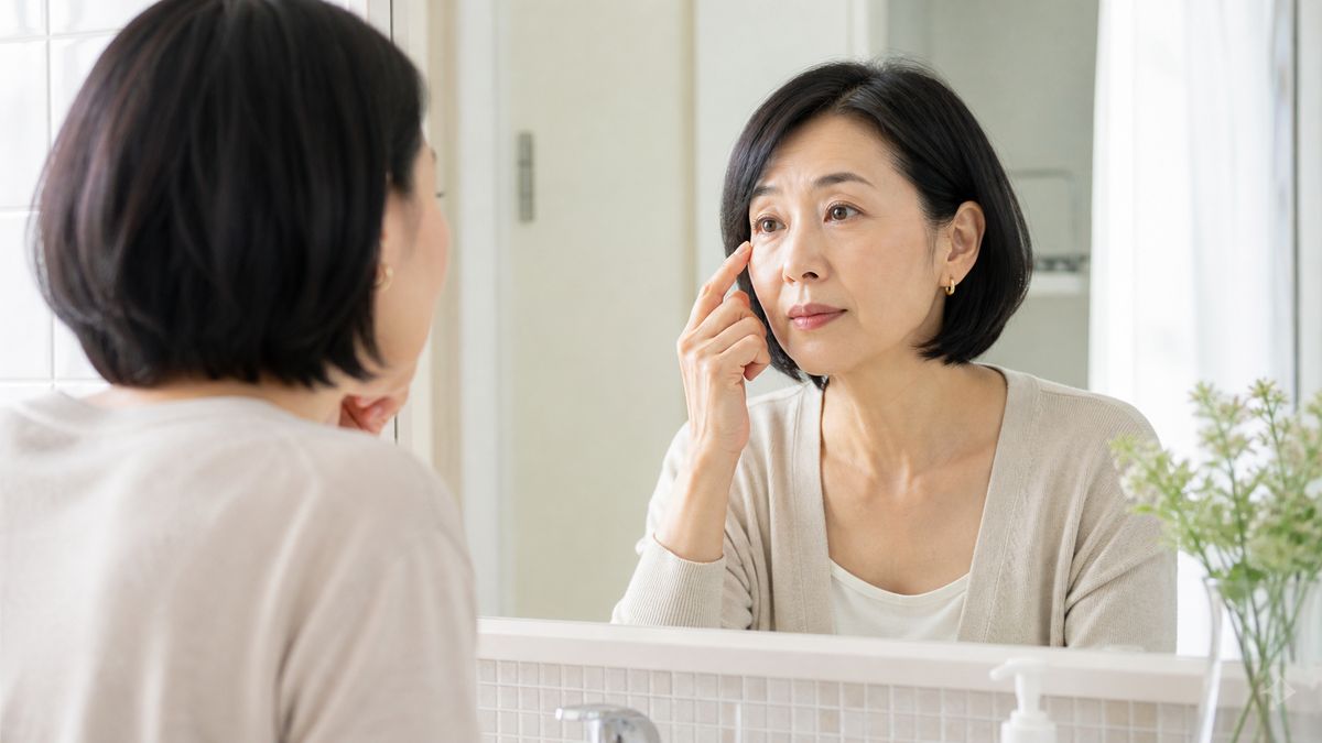 洗面所の鏡越しに自分の目元を確認する女性