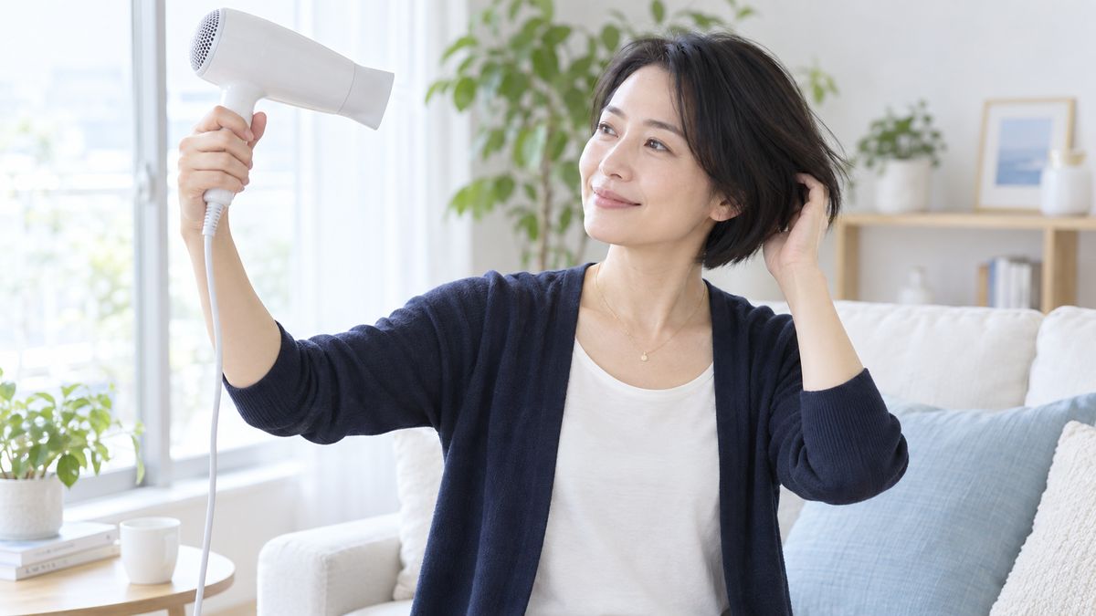 窓辺でドライヤーを離して髪を乾かす女性