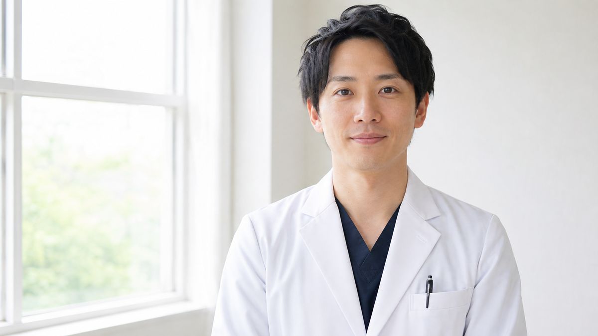 診察室の窓辺で正面を向く白衣の男性医師