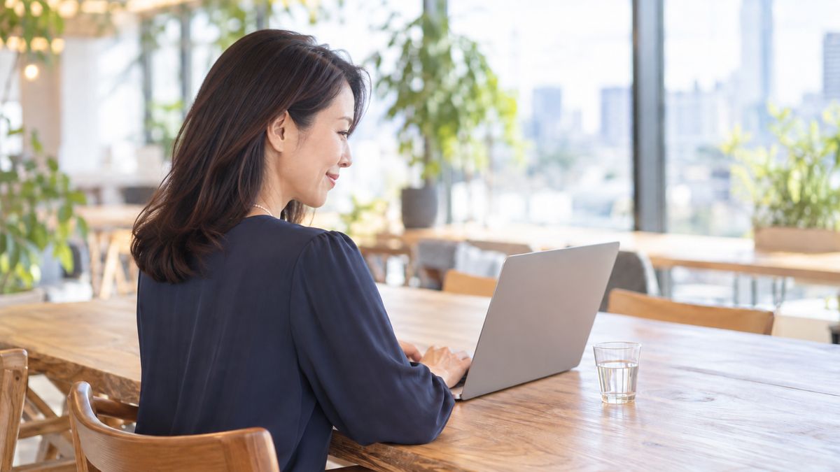 コワーキングスペースでノートパソコンに向かい微笑む女性