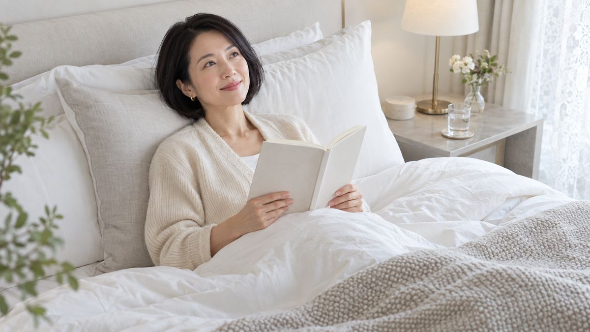 ベッドで枕にもたれて本を読む女性
