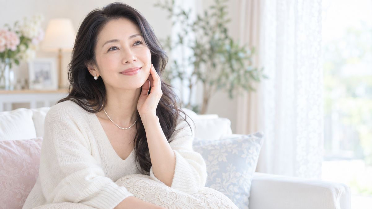 ソファでフェイスラインに指先を添えて微笑む女性