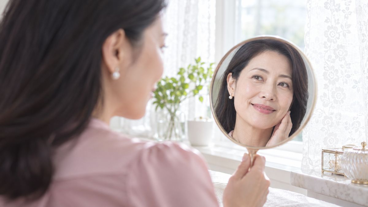 窓辺で手鏡をのぞいて微笑む女性