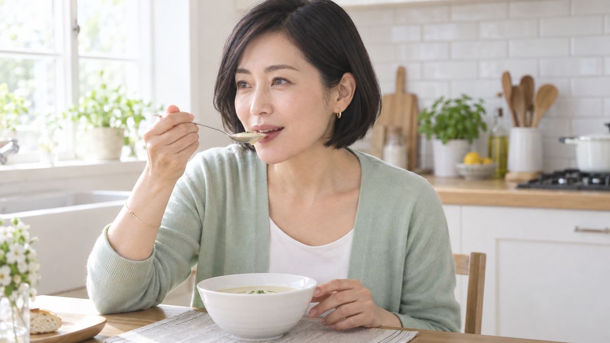 キッチンでスプーンでスープを口に運ぶ女性