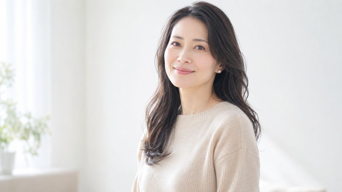 白い室内で自然光を受けて立つセミロングの女性
