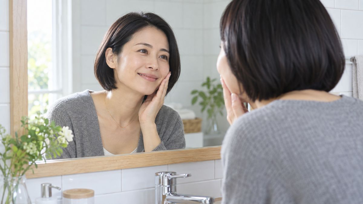 洗面所の鏡に向かい頬に手を添えて微笑むボブヘアの女性