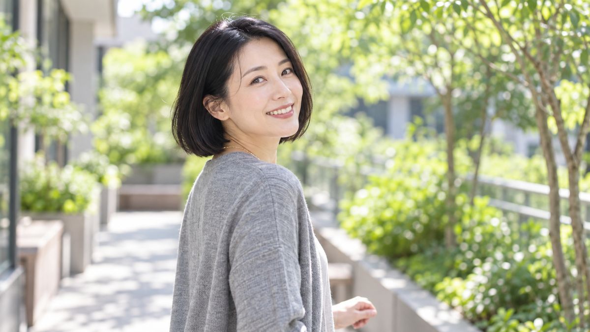 緑に囲まれた屋外テラスを歩きながら振り返る女性