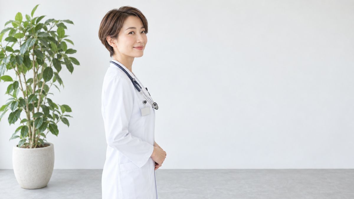 観葉植物の横に横向きで立つ白衣の女性医師