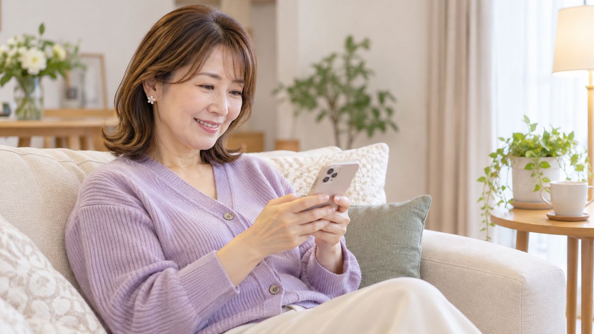 ソファでスマートフォンに文字を入力して微笑む女性