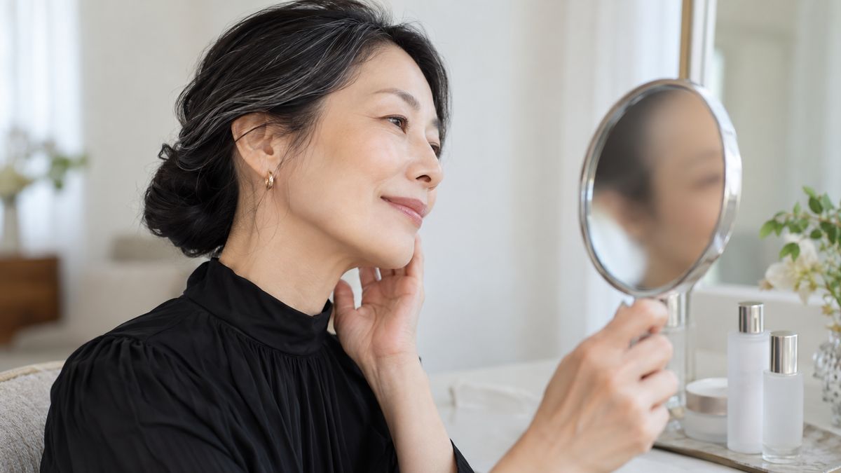 ドレッサーの前で手鏡を持ち横顔を確かめる女性