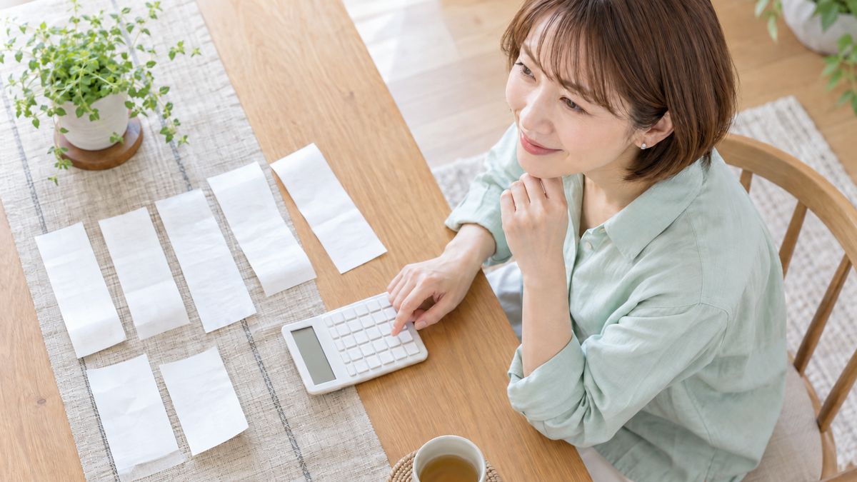 ダイニングテーブルで領収書を並べて電卓で計算する女性の手元