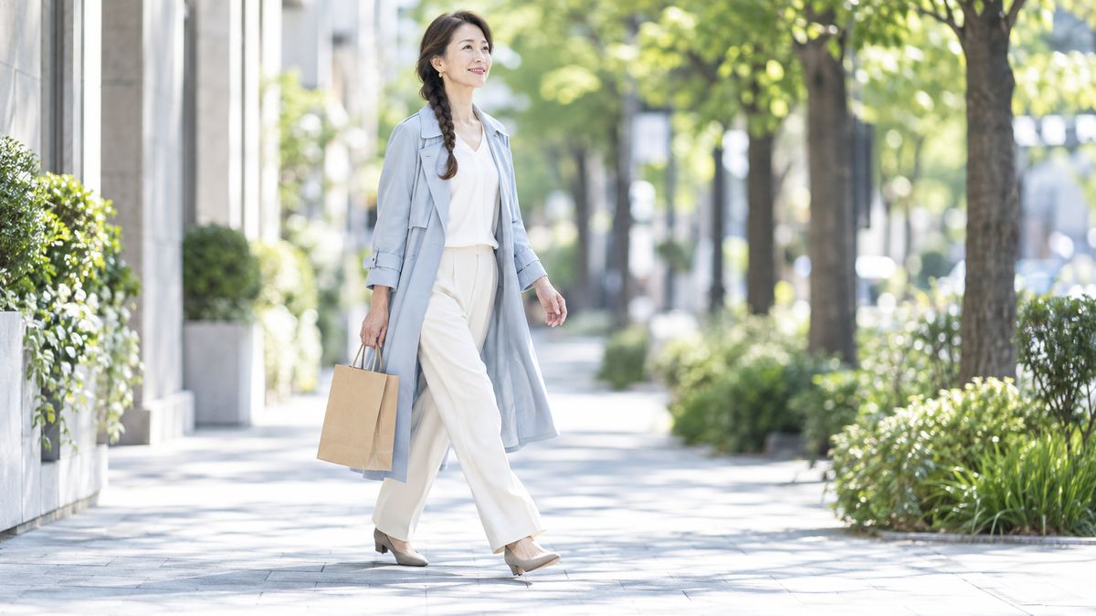 街路樹のある歩道を紙袋を手に歩く三つ編みの女性