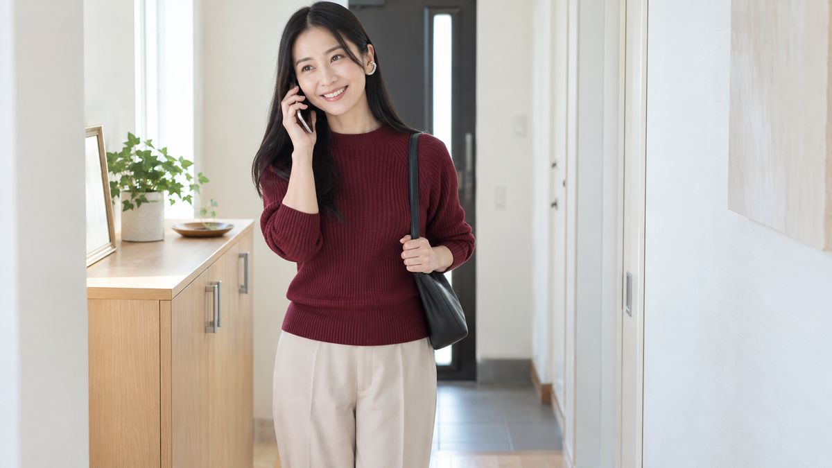 自宅の廊下でスマートフォンを耳に当てて微笑む女性