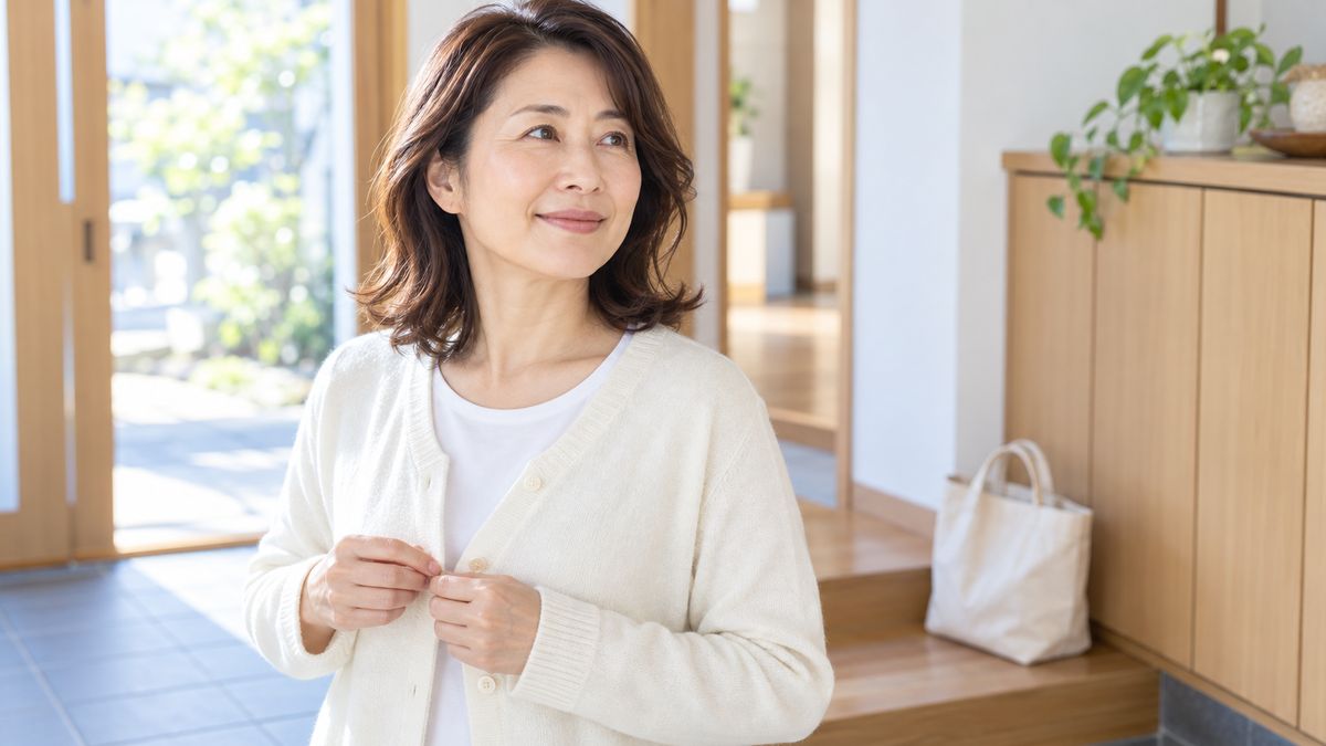 玄関でカーディガンのボタンを留めながら微笑む女性