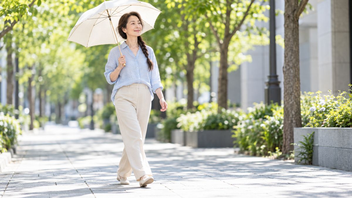 街路樹の歩道を日傘を差して歩く三つ編みの女性