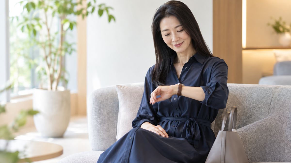 待合のソファに座り腕時計を見て微笑む女性