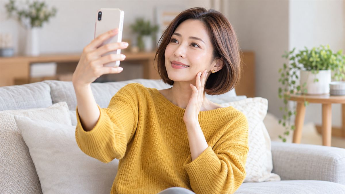 ソファでスマートフォンを顔の前に掲げて微笑む女性