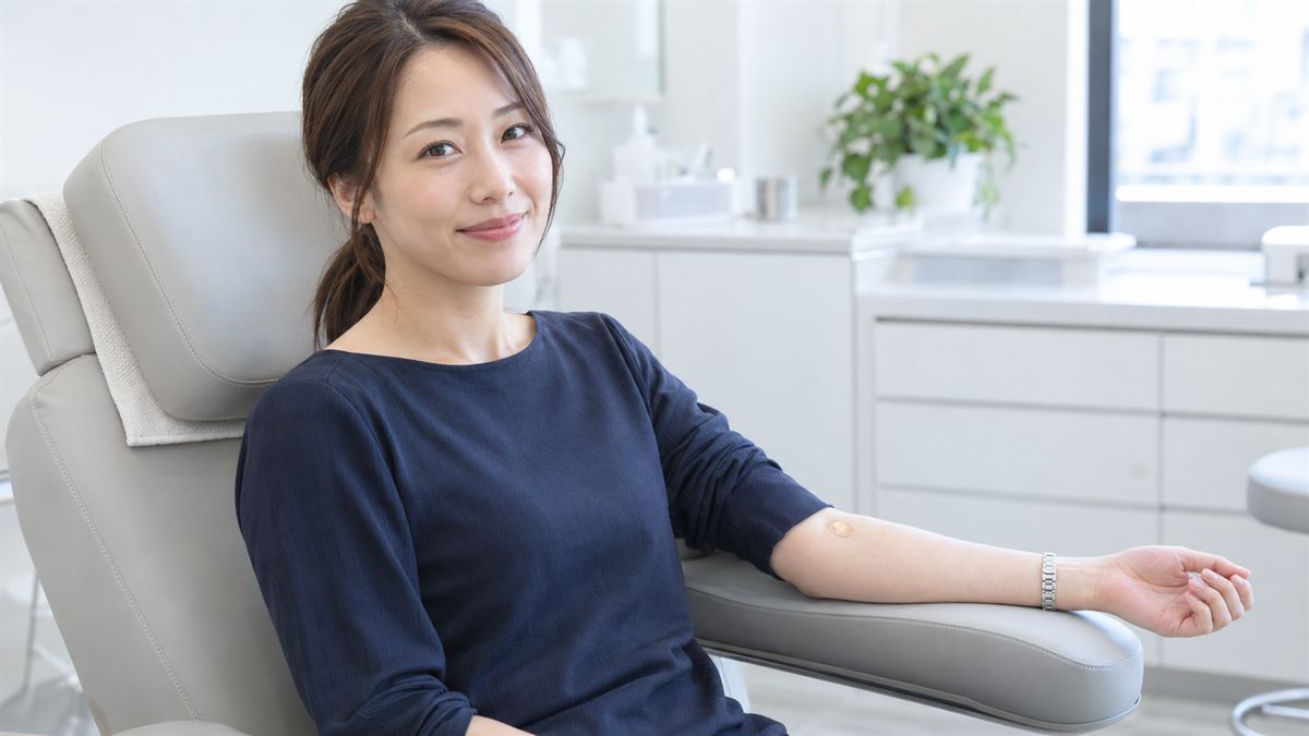 ひじの内側に絆創膏を貼り処置用チェアで微笑む女性